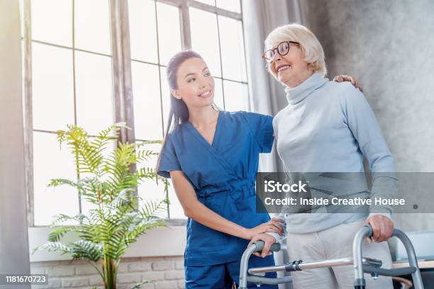 Female Asian Nurse Helping Senior Woman To Walk With Walker At Home Stock Photo - Download Image Now