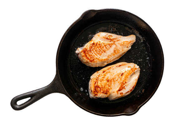 istock Two whole chicken breasts roasting in cast iron pan isolated on white. Top view. 1181673080