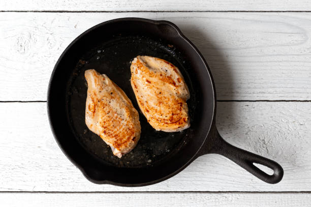 istock Two whole chicken breasts roasting in cast iron pan isolated on white. Top view. 1181673282