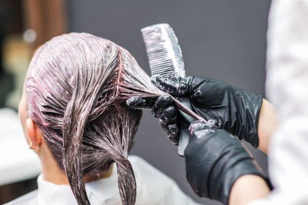 Close up of hairdresser hands is coloring woman's hair in black gloves. Close up back view of hairdresser is applying color to customer's hair in black gloves. Hair coloring in a beauty salon. Beauty and people concept. dye stock pictures, royalty-free photos & images