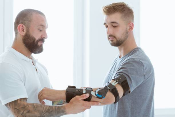 physiothérapeute tatoué qui met une orthèse sur la main d'un jeune patient après un accident - orthèse photos et images de collection