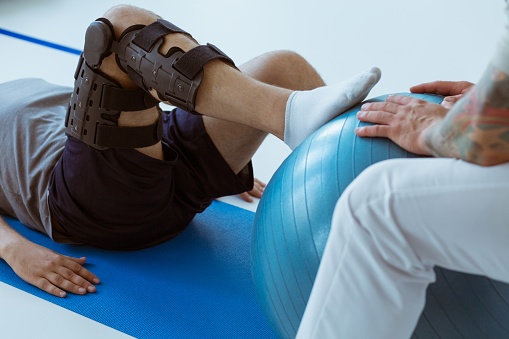 Bastante paciente sentado en la alfombra azul en el gimnasio y entrenando con la pelota photo