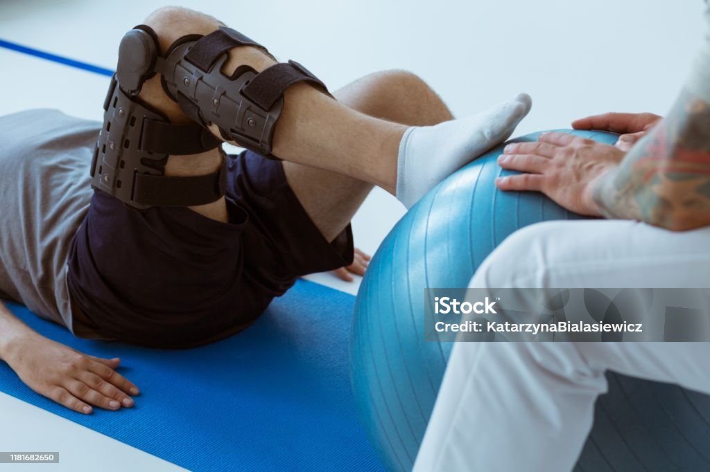 Pretty patient sitting on the blue mat in the gym and training with the ball Physical Therapy Stock Photo