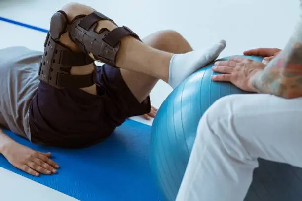 Photo of Pretty patient sitting on the blue mat in the gym and training with the ball