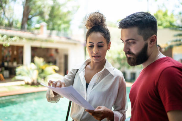 Real estate agent showing papers and talking to a clinet while visitng a house stock photo