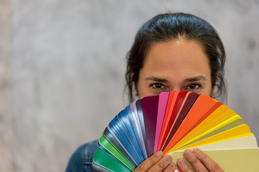 Beautiful woman holding a color swatch looking at camera with playful eyes - Lifestyles
