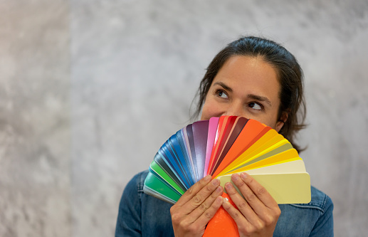 Adult woman holding a color swatch looking uo daydreaming - Lifestyles
