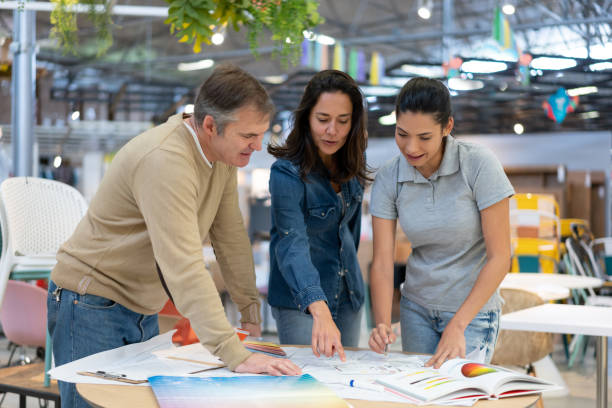 istock Young female interior designer suggesting different things while pointing at a sketch to customer couple at a furniture store 1181691075