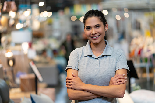 Confident female manager of a furniture store looking at camera smiling with arms crossed - Focus on foreground