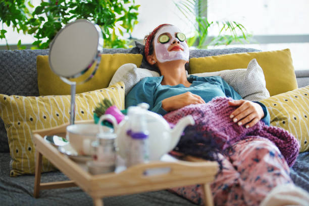 Pampering myself on weekends. Young woman with a mask and rolls of cucumber on her face is enjoying a morning weekend. body care stock pictures, royalty-free photos & images