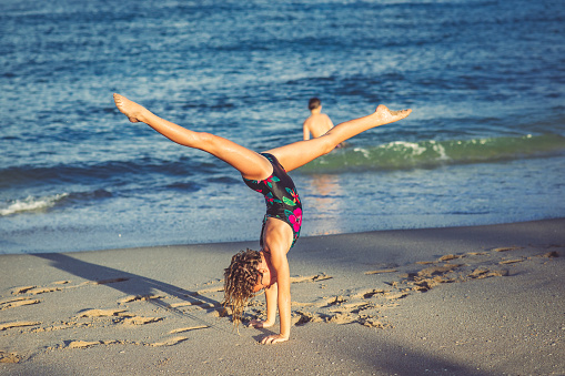 Beautiful young girl practices backbends and gymnastic loves at the beach. She is about 10 years old in swimwear perhaps on vacation, limber and athletic