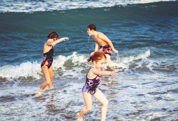 istock Siblings, three children, play in the ocean having fun getting hit by waves 1181726302