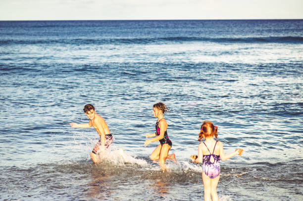 istock Siblings, three children, play in the ocean having fun getting hit by waves 1181726406