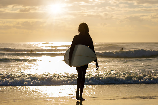 African-Australian Female Surfer Leaving The Surf At Sunrise At Australian Beach