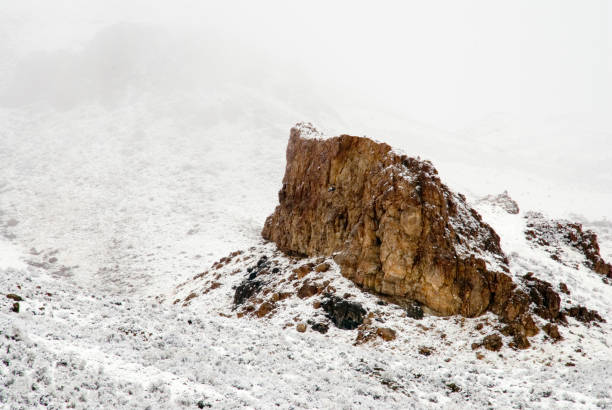 Brown flat Rock face erupting out of the snow hillside in front of a misty background in the Owyhee County backcountry in Idaho