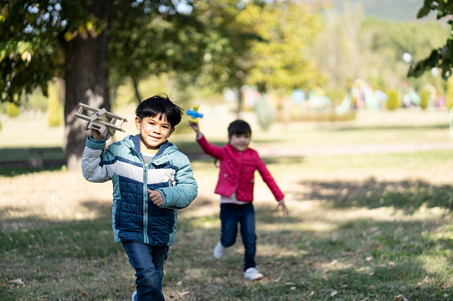 Little boy and girl playing in park, running.