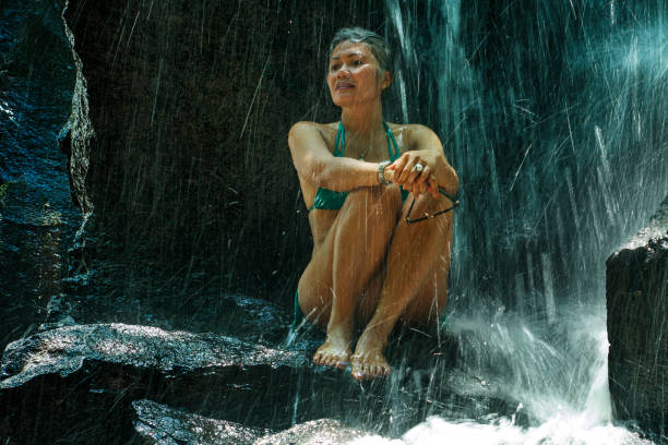 attraente e felice donna adulta con i capelli grigi anni '40 o '50 godendo beato e libero nella bellissima cascata tropicale sentendo la purezza e la bellezza della natura bagnata sotto l'acqua che cade - waterfall zen like women meditating foto e immagini stock