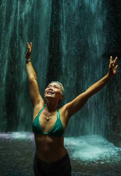 attraktive und glückliche mitte erwachsene frau mit grauen haaren 40er oder 50er jahre genießen glückselig und frei am schönen tropischen wasserfall gefühl der reinheit und schönheit der natur nass unter dem fallenden wasser - waterfall water nature zen like stock-fotos und bilder