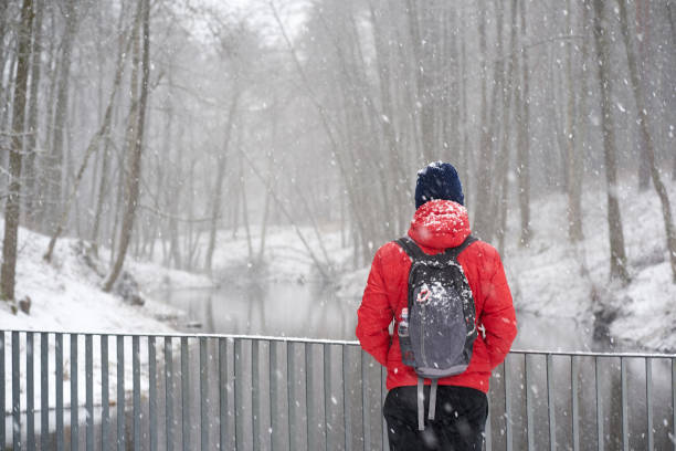 istock Man traveler dressed in red jacket enjoying snowfall standing backfront on bridge near river 1181772265