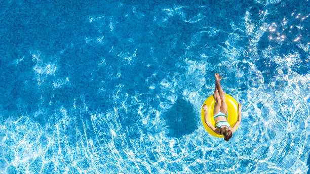 active young girl in swimming pool aerial top view from above, child relaxes and swims on inflatable ring donut and has fun in water on family vacation, tropical holiday resort - blue water swimming pool sports and fitness imagens e fotografias de stock