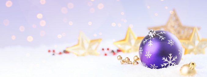 Purple christmas ball with decoration on the snow over blurry background.