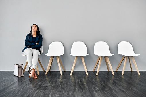 Studio shot of a young businesswoman looking annoyed while waiting in line against a grey background