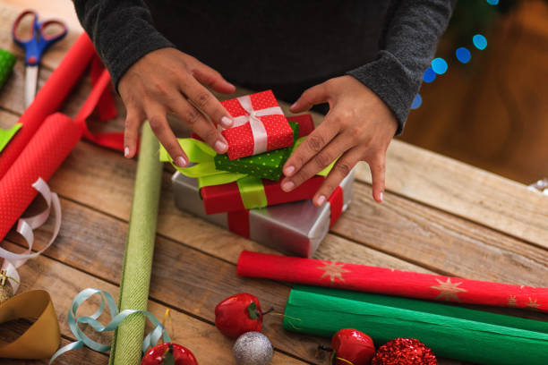 Young woman wrapping Christmas presents using decorative gift boxes, real people, obscured face