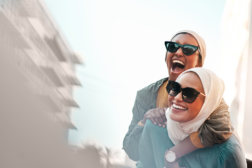 Cropped shot of an attractive young woman wearing sunglasses and a headscarf while giving her female friend a piggyback ride