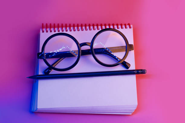 istock black round glasses lie on a Notepad in neon light on pink background 1181807962