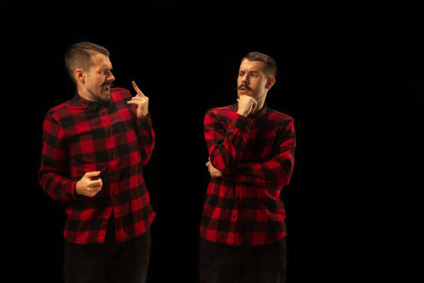 Young handsome man arguing with himself on black studio background. Concept of human emotions, mental issues, internal conflict, split personality. Half lenght portrait. Negative space.