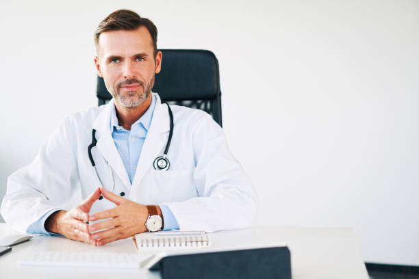 istock Handsome doctor sitting in office and smiling gently at camera 1181808969