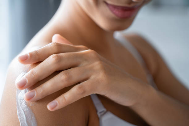 Pleased female rubbing a lotion into the arm Cropped photo of a smiling young woman rubbing a body lotion into the arm Combing stock pictures, royalty-free photos & images