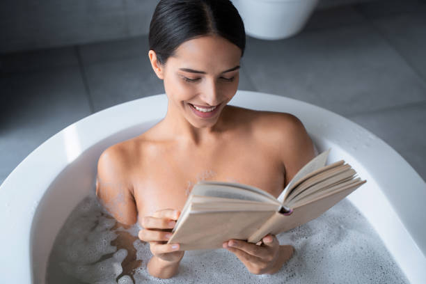 istock Happy lady reading a book in the bathroom 1181813472