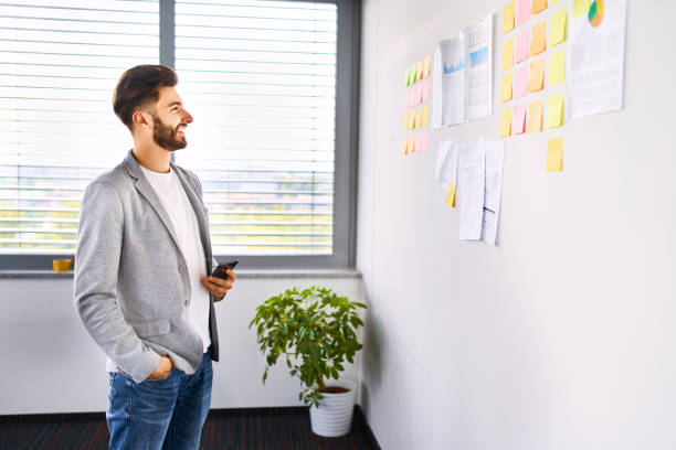 istock Smiling young businessman standing in office looking at notes on wall 1181815667