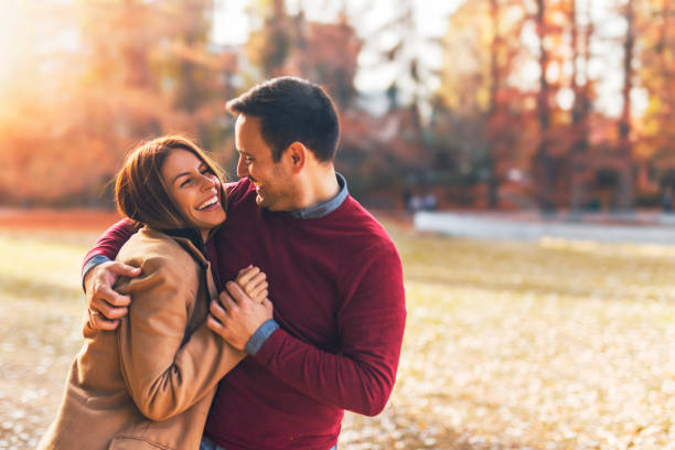 feliz pareja en el parque público en otoño - abrazar fotos fotografías e imágenes de stock