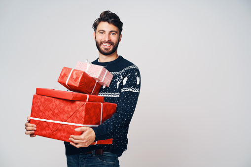 Young man holding stack of Christmas presents, smiling at camera, isolated.