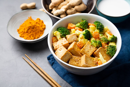 Vegan Stir-fry Tofu with broccoli vegetables, rice noodles and chili in teriyaki glaze sauce on dark wood