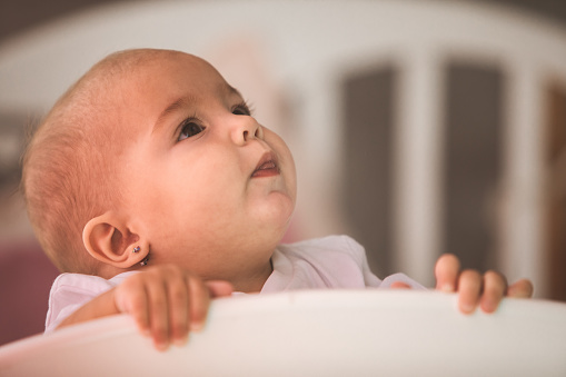 Portrait of a cute baby girl sticking out tongue and looking up in a crib.