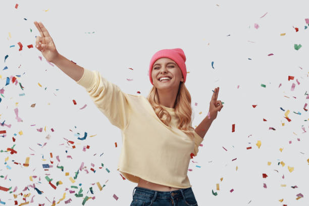 istock Attractive young woman smiling while standing against grey background with confetti flying around 1181824163