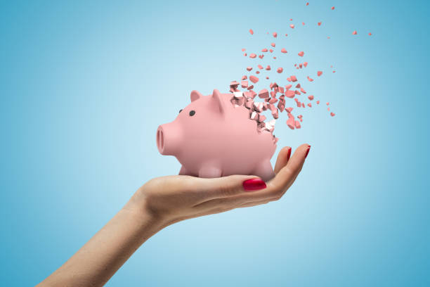 Close-up of woman's hand facing up and holding cute pink piggy bank that has started to disintegrate into pieces on light-blue background. stock photo