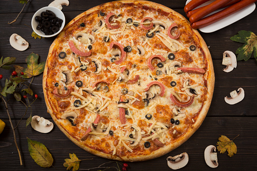 Italian traditional pizza with sausages and mushrooms and olive. Fast food for lunch.