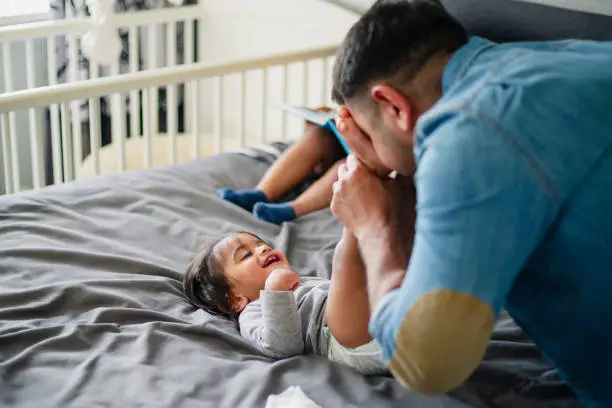 A side-view shot of a father playing on the bed with his young son, they are having fun together.
