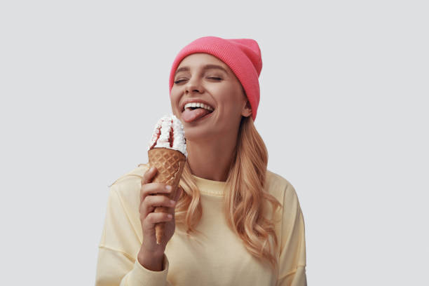 istock Attractive young woman eating ice cream and making a face while standing against grey background 1181825376