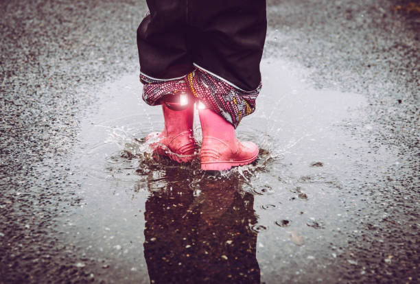 재미, 젖은 거리에 물 웅덩이에 점프, 반사 세부 직물 줄무늬 빛나는 레인 부츠를 입고. 어두운 개념에서 높은 가시성과 안전. - puddle rain child splashing 뉴스 사진 이미지