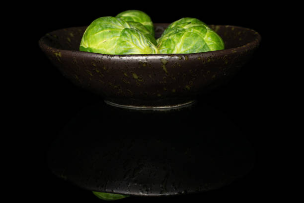 Group of three whole fresh green brussels sprout on glazed bowl isolated on black glass