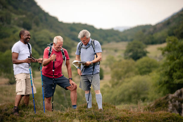 Senior Group Of Men Looking At Map Small group of senior friends out walking with walking poles in Cumbria. orienteering stock pictures, royalty-free photos & images