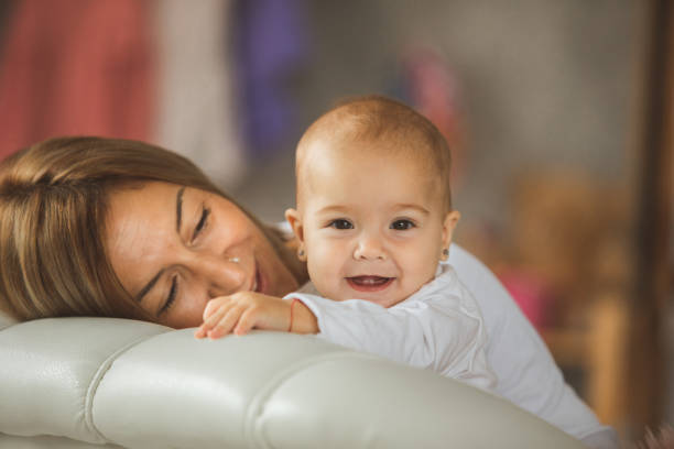 Mid adult Caucasian mother and cute baby girl playing at sofa, having fun.