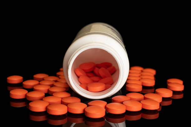 Lot of whole orange tablet pharmacy in bottle and near isolated on black glass