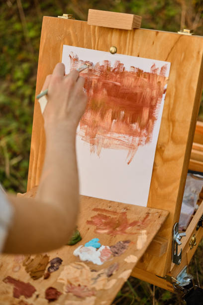 istock Easel with a child's drawing in nature. The hand is visible in the frame 1181851382