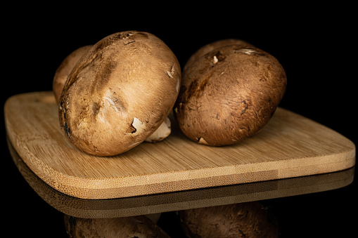 Group of three whole fresh brown mushroom champignon on bamboo cutting board isolated on black glass